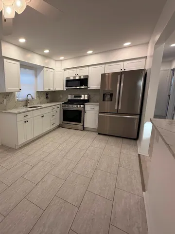 a large white kitchen with stainless steel appliances granite countertop a sink and white cabinets