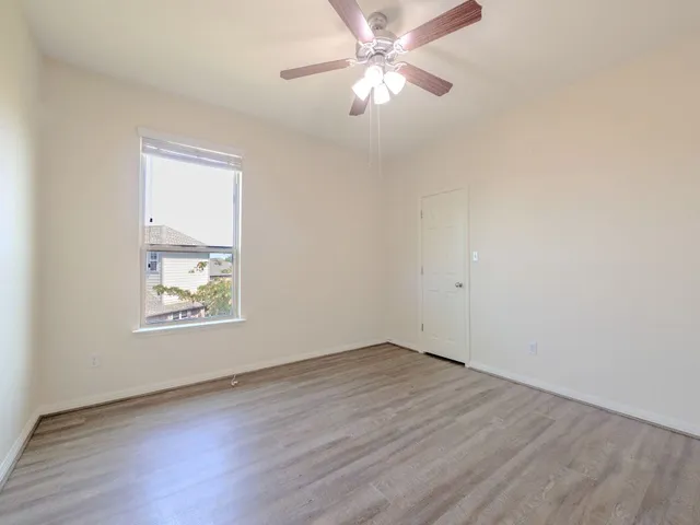 an empty room with wooden floor ceiling fan and windows