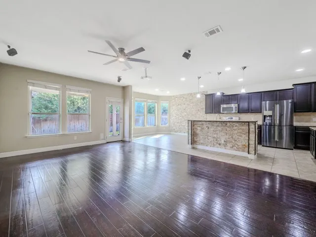 an empty room with wooden floor kitchen view and a window