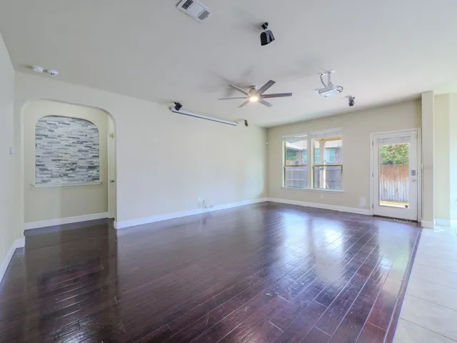 an empty room with wooden floor chandelier fan and windows