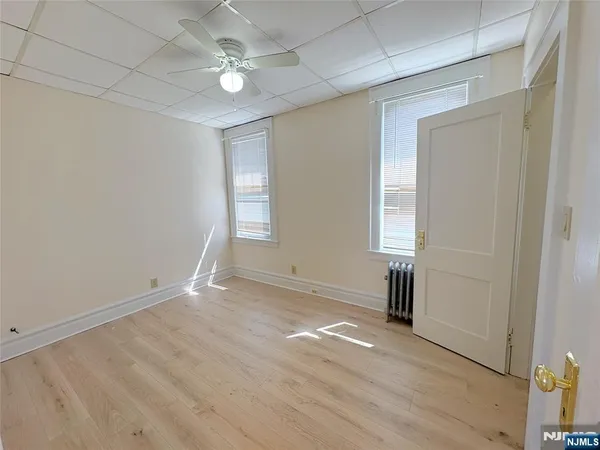 an empty room with wooden floor ceiling fan and windows