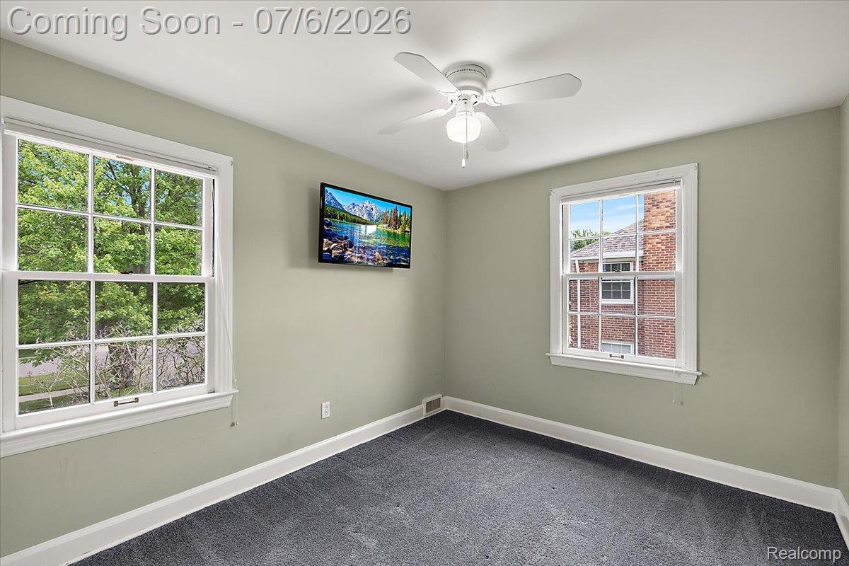 1051 Devonshire Road Grosse Pointe, MI 48230 - Photo 41 of 98 Room featuring two double-hung windows with white trim, a white ceiling fan with light fixture, light gray wall paint, and dark gray carpet flooring
