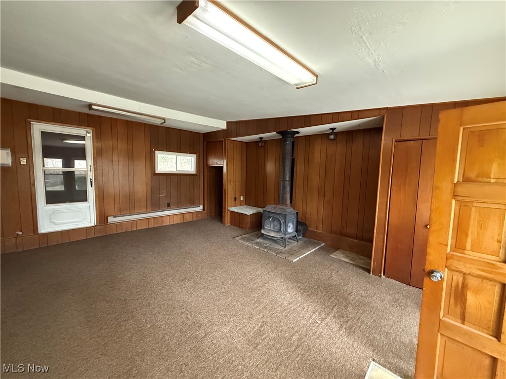 3122 South Medina Line Road Wadsworth, OH 44281 - Photo 39 of 41 Unfurnished room with a baseboard radiator, wood walls, a wood stove, and carpet floors