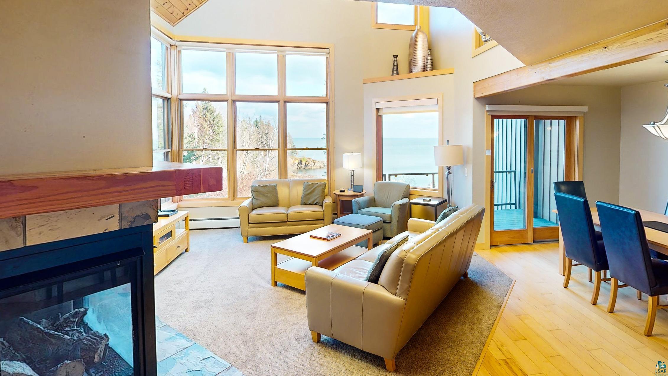 40 Surfside Drive, Unit 5D Tofte, MN 55615 - Photo 26 of 37 Open-concept living area featuring a stone-surround fireplace with a wood mantle, an expansive window wall, a dining area with wood-finish flooring, and a sliding glass door providing outdoor access