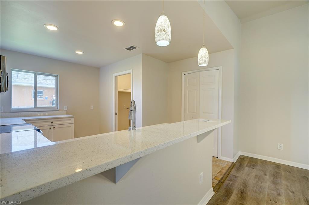 8381 Blackberry Road Fort Myers, FL 33967 - Photo 4 of 36 Kitchen with hardwood / wood-style floors, light stone counters, a kitchen bar, and pendant lighting