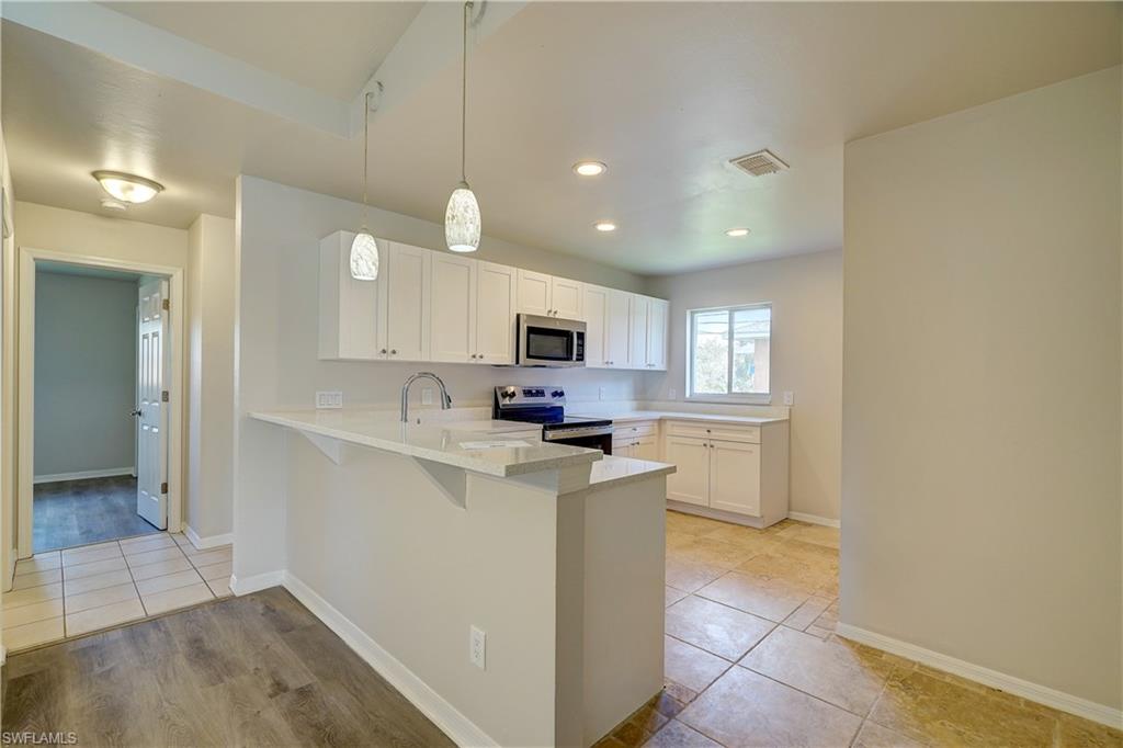 8381 Blackberry Road Fort Myers, FL 33967 - Photo 5 of 36 Kitchen featuring kitchen peninsula, white cabinets, hanging light fixtures, appliances with stainless steel finishes, and a breakfast bar