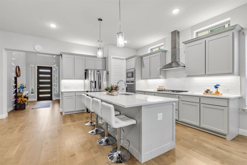 7852 Buffaloberry Road Frisco, TX 75035 - Photo 6 of 36 Open-concept kitchen featuring light wood-finish flooring, a large island with seating, grey cabinetry, stainless steel appliances, and a white subway tile backsplash