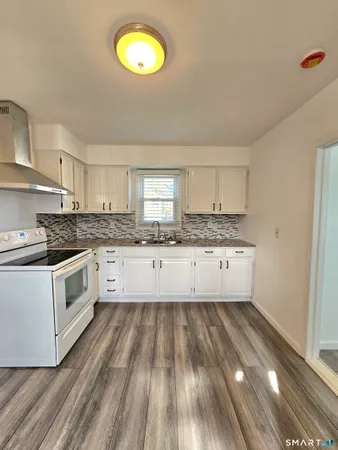 a large white kitchen with granite countertop a stove top oven a sink with wooden floors