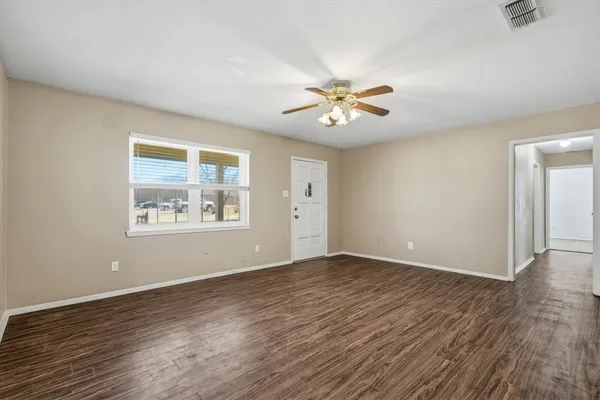 an empty room with wooden floor chandelier fan and windows