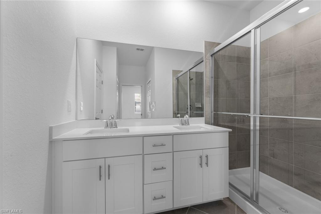 2856 Citrus Street Naples, FL 34120 - Photo 13 of 20 Full bath with double vanity, a stall shower, a textured wall, and dark tile patterned floors