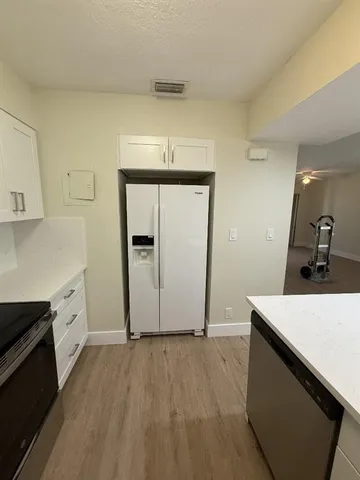a kitchen with a sink dishwasher a refrigerator and white cabinets with wooden floor