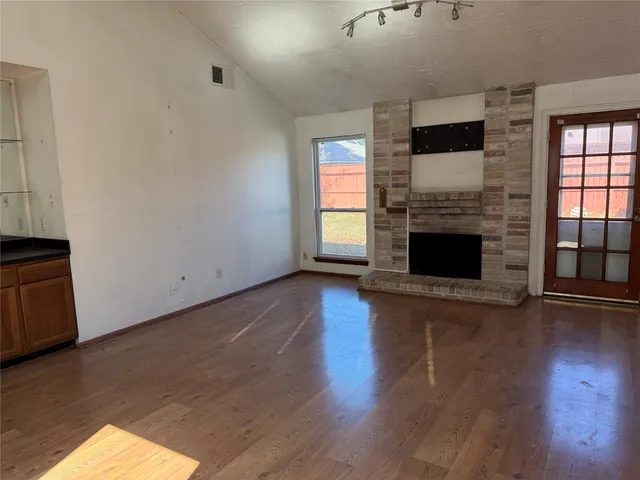 an empty room with wooden floor fireplace and windows