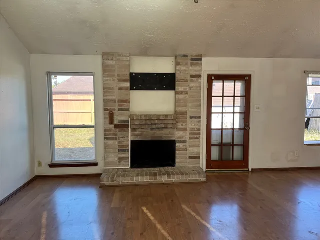 an empty room with wooden floor fireplace and windows