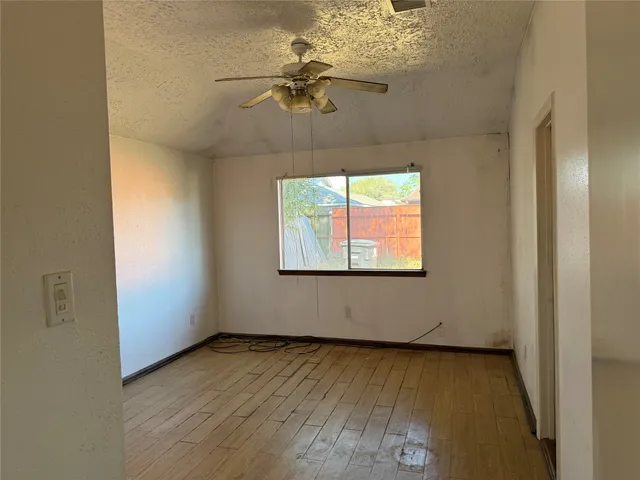 an empty room with wooden floor chandelier fan and windows