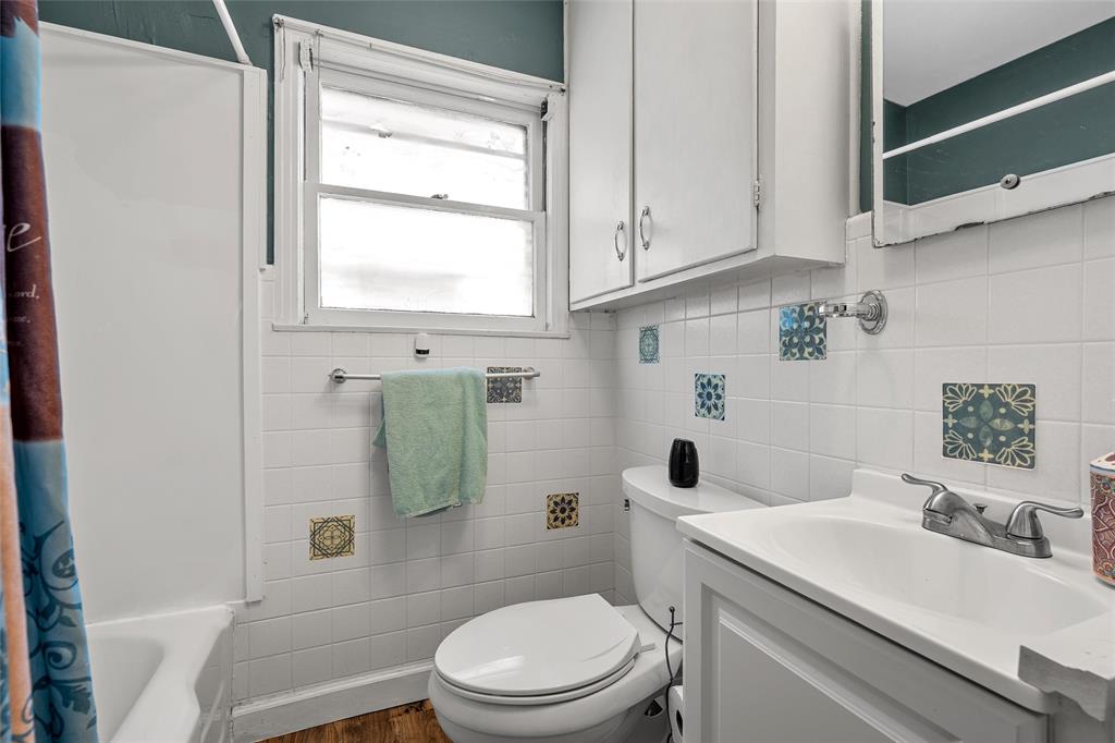 301 North 40th Street Waco, TX 76710 - Photo 14 of 26 Bathroom featuring white ceramic wall tiling with accent tiles, a white vanity with integrated sink, a white toilet, and a window with white trim