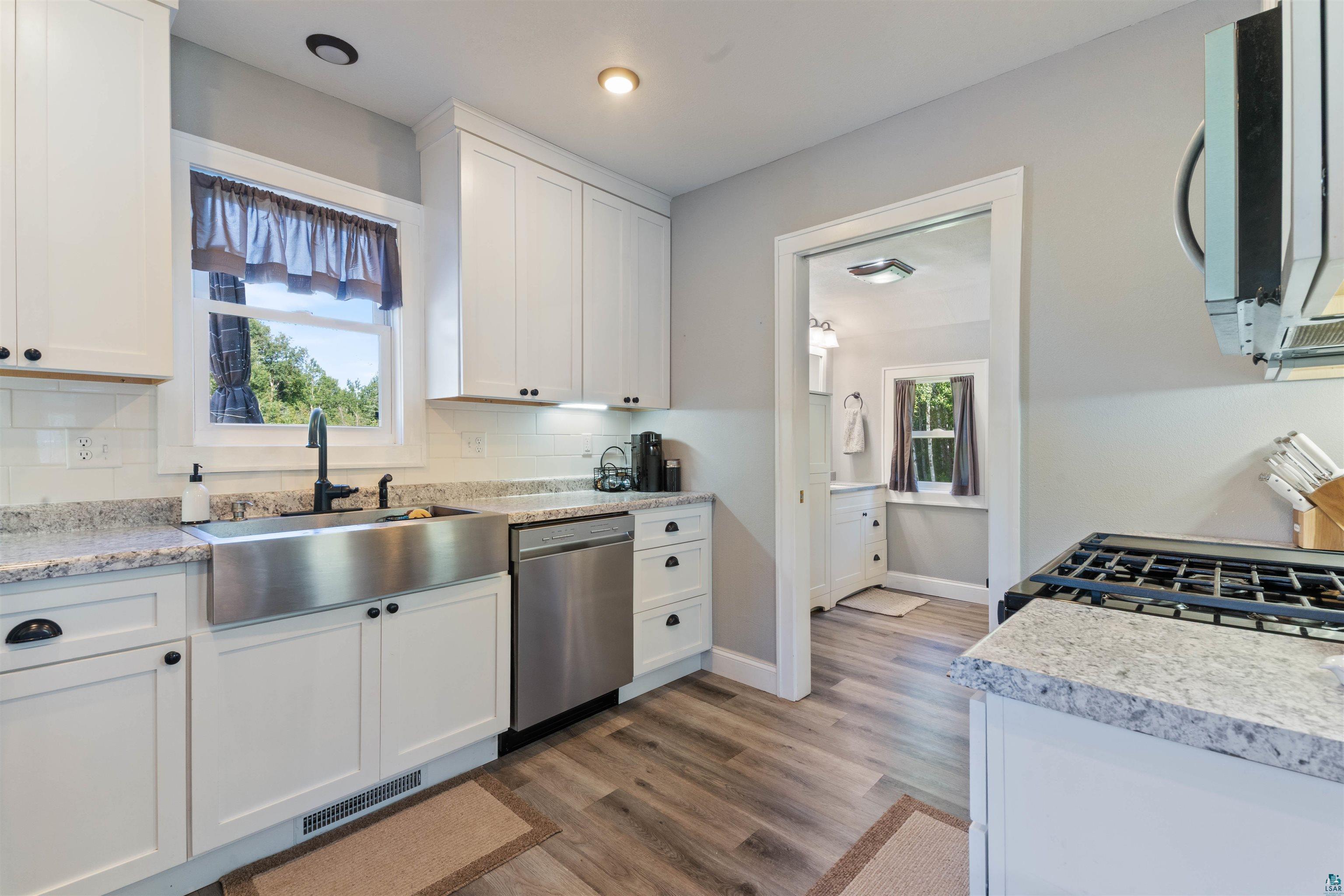 3835 South County Rd K South Range, WI 54874 - Photo 9 of 29 Modern kitchen featuring white shaker cabinetry, stainless steel farmhouse sink with a matte black faucet, light granite countertops, a subway tile backsplash, and wood-finish flooring