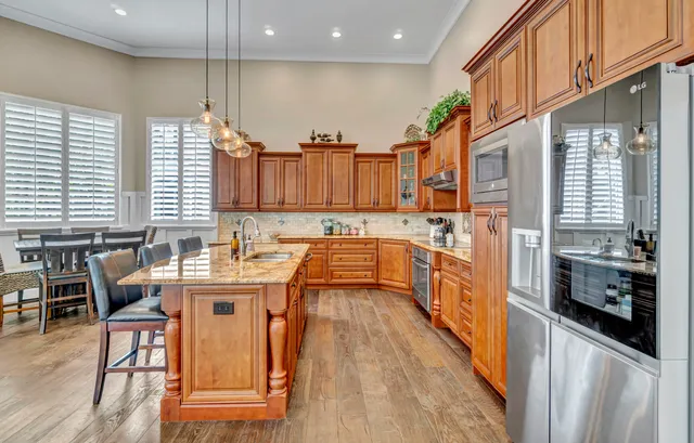 a kitchen with stainless steel appliances granite countertop stove a refrigerator a kitchen island a dining table and chairs with wooden floor