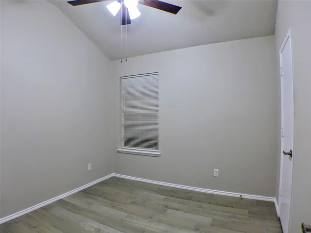 an empty room with wooden floor chandelier fan and windows