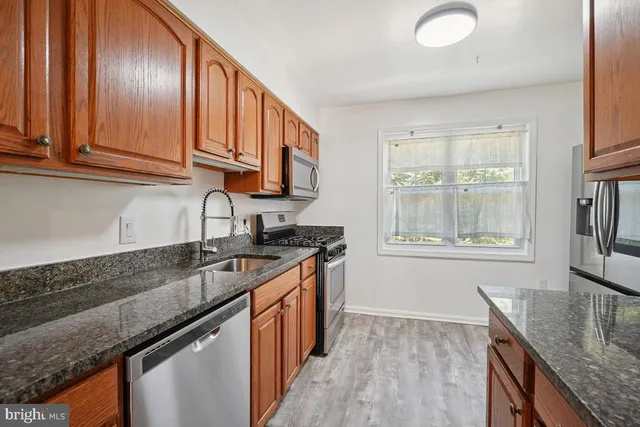 a kitchen with granite countertop stainless steel appliances a sink window and cabinets
