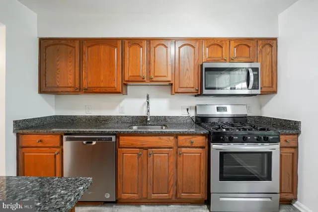 a kitchen with granite countertop wood cabinets stainless steel appliances and a sink