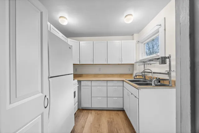 a kitchen with a sink a refrigerator a window and white cabinets