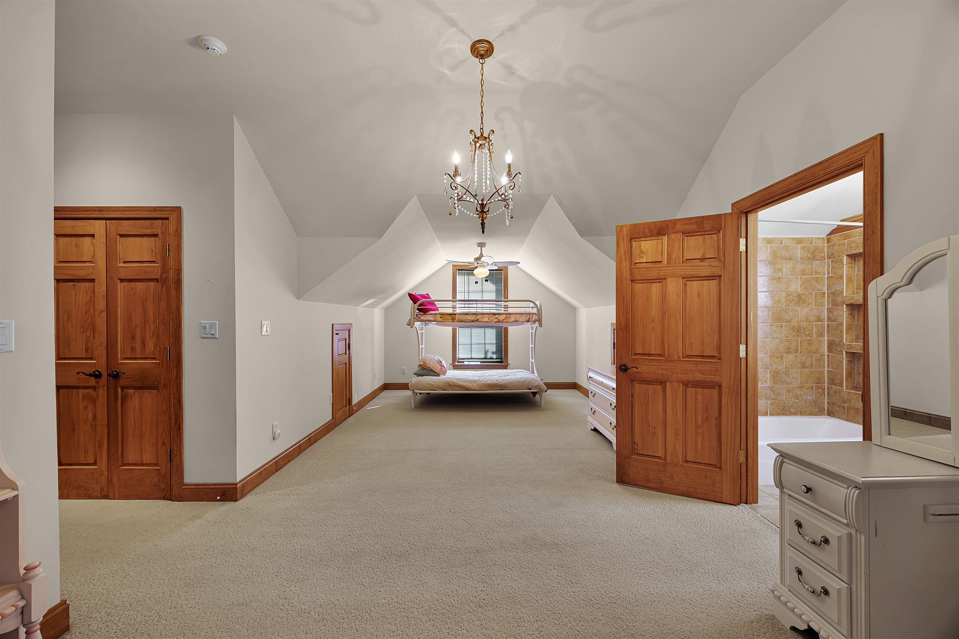 Unfurnished bedroom with light carpet, ensuite bath, lofted ceiling, and an inviting chandelier