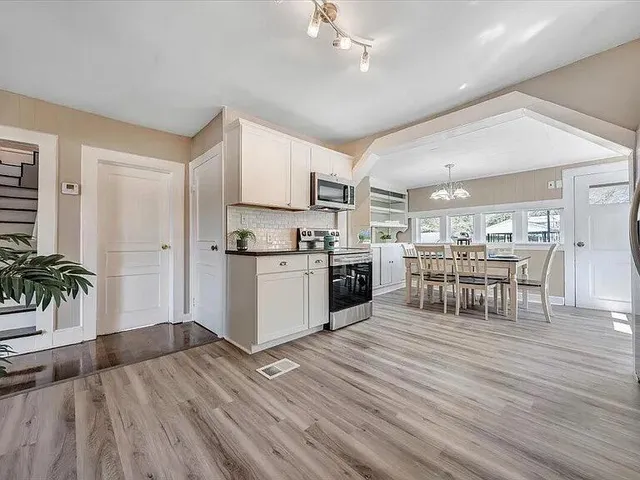 a kitchen with stainless steel appliances granite countertop a stove top oven a sink dishwasher a dining table and chairs with wooden floor