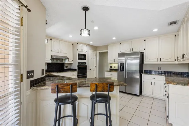 a kitchen with stainless steel appliances kitchen island granite countertop a refrigerator a stove a sink a dining table and chairs with wooden floor