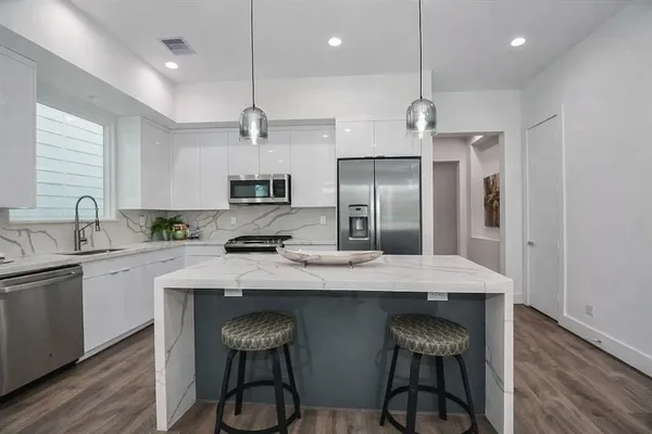 a kitchen with stainless steel appliances granite countertop a sink a stove a refrigerator and island with wooden floor