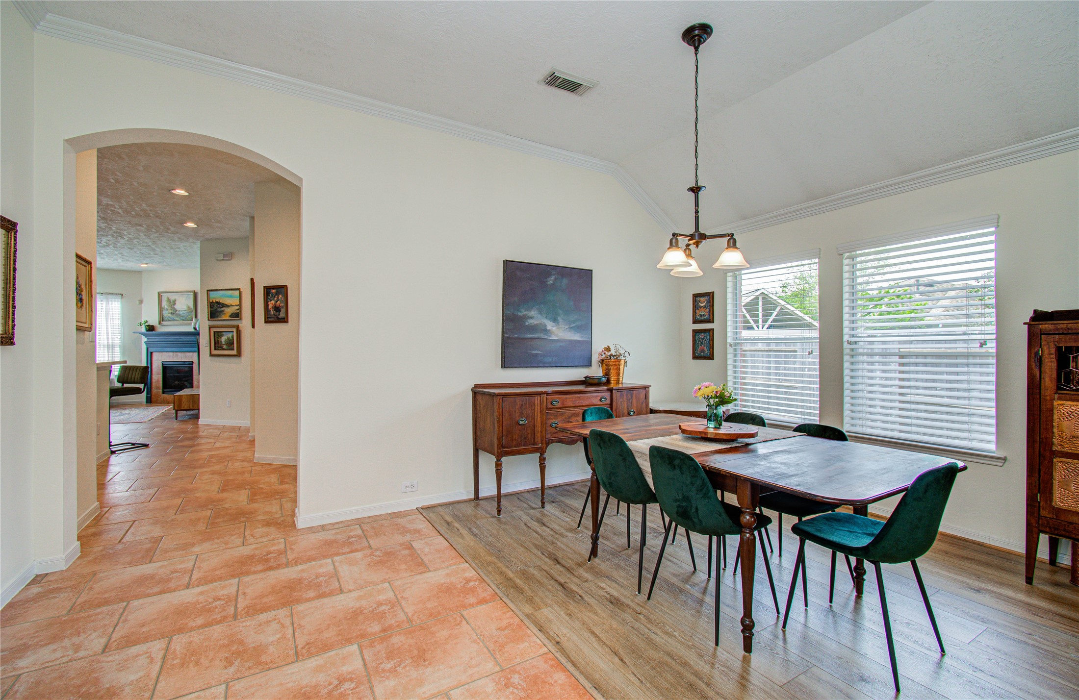 20007 Alcea Court Spring, TX 77379 - Photo 8 of 36 This photo showcases a bright dining area with a vaulted ceiling and large windows, providing ample natural light. The space features a mix of tile and wood flooring, with a cozy adjacent living room visible through an archway.