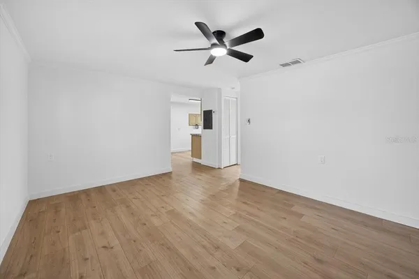a view of an empty room with wooden floor and a ceiling fan