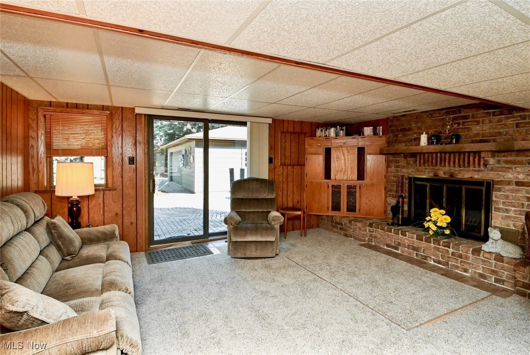 5653 Dailey Road New Franklin, OH 44319 - Photo 9 of 24 Unfurnished living room featuring a paneled ceiling, wood walls, carpet, and a brick fireplace