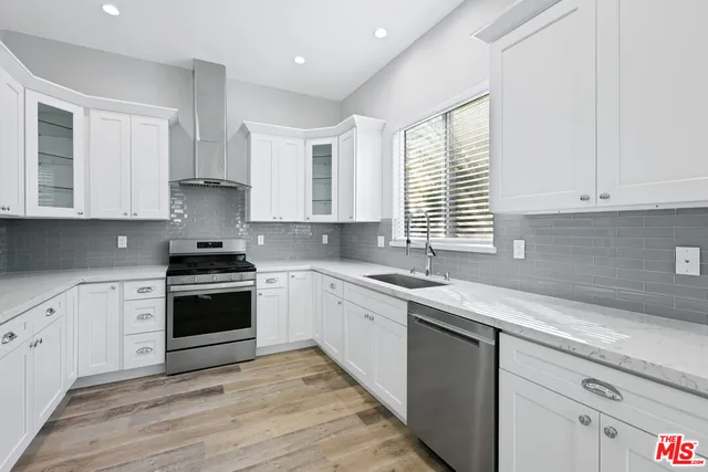 a kitchen with stainless steel appliances granite countertop a sink a stove a refrigerator white cabinets and wooden floor