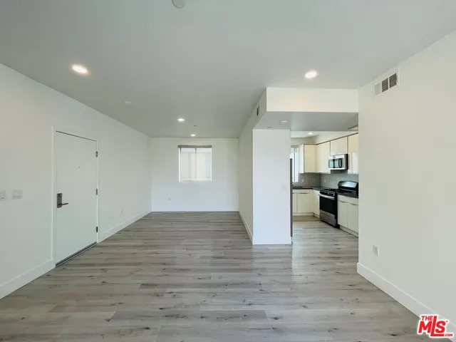 an empty room with wooden floor and a kitchen