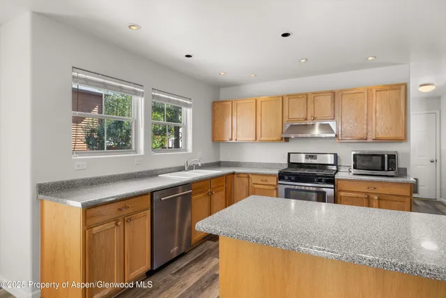 a kitchen with stainless steel appliances granite countertop a refrigerator a sink dishwasher a stove and white countertops with wooden floor