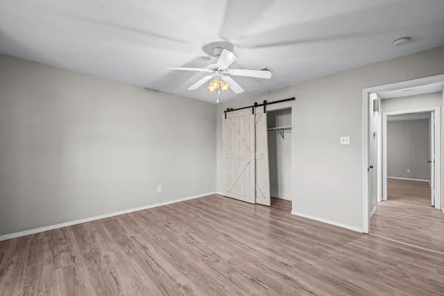 an empty room with wooden floor fan and windows