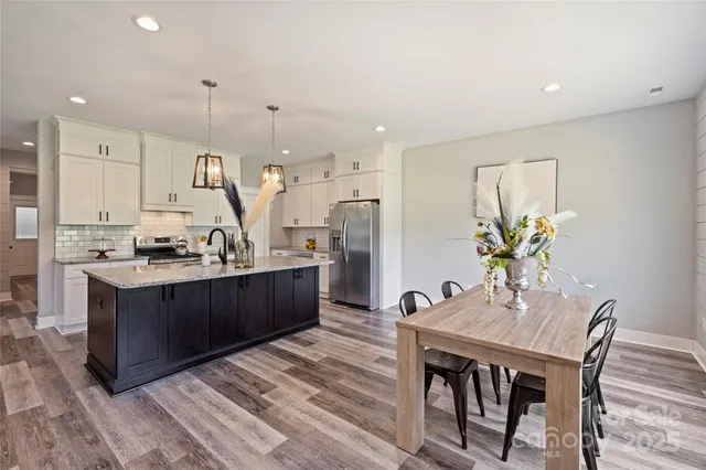 a kitchen with stainless steel appliances kitchen island granite countertop a table chairs and a refrigerator