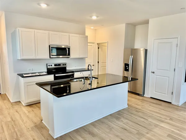 a kitchen with stainless steel appliances a sink a stove top oven a refrigerator cabinets and wooden floor