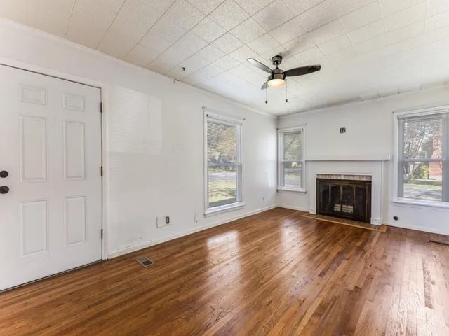 a view of an empty room with wooden floor fireplace and a window