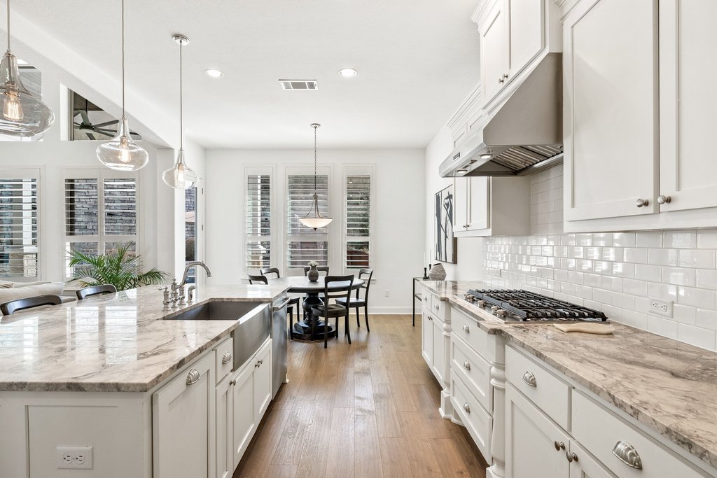 5812 Davenport Divide Road Austin, TX 78738 - Photo 17 of 40 White cabinetry extends to the ceiling, paired with subway tile backsplash and a professional-style gas range beneath a stainless vent hood. Abundant drawer storage and expansive prep space make this a kitchen built for real use.
