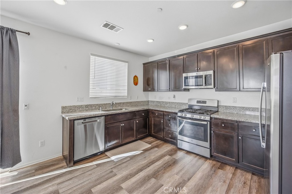 925 Bluebell Way Beaumont, CA 92223 - Photo 11 of 33 a kitchen with stainless steel appliances granite countertop a stove top oven a sink and dishwasher a refrigerator with wooden floors