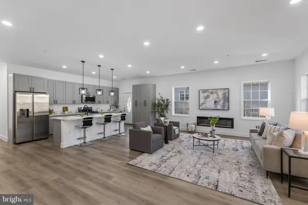 a living room with stainless steel appliances furniture wooden floor and a kitchen view