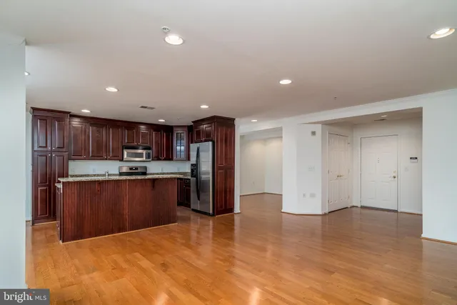 a kitchen with stainless steel appliances kitchen island granite countertop a refrigerator a stove top oven and a sink with wooden floor