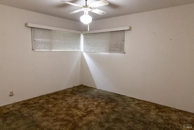 an empty room with a chandelier fan and windows