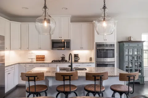 a kitchen with stainless steel appliances kitchen island granite countertop a stove top oven a sink a dining table and chairs with wooden floor