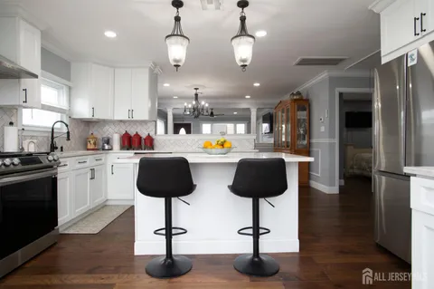 a kitchen with stainless steel appliances granite countertop a refrigerator a sink dishwasher a stove and a dining table with wooden floor