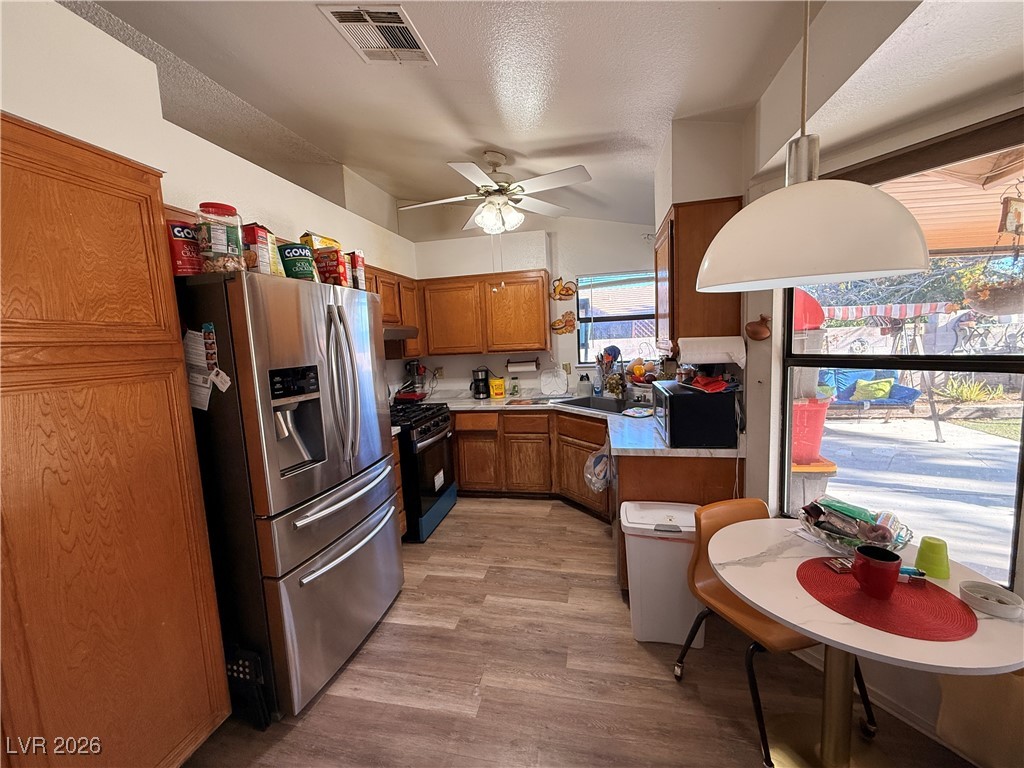 6425 West Eagle Point Road Las Vegas, NV 89108 - Photo 23 of 42 Kitchen with brown cabinetry, appliances with stainless steel finishes, light countertops, lofted ceiling, and light wood-style floors