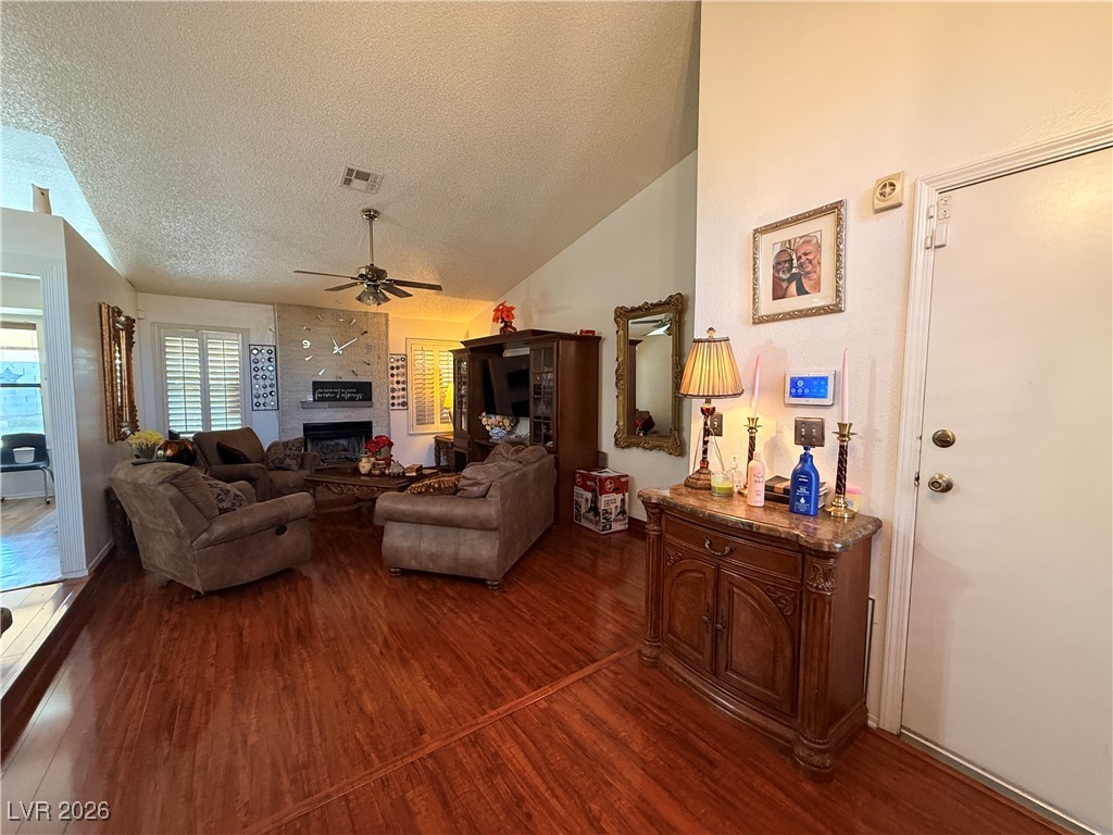 6425 West Eagle Point Road Las Vegas, NV 89108 - Photo 8 of 42 Living room featuring lofted ceiling, dark wood-style flooring, a ceiling fan, a textured ceiling, and a large fireplace