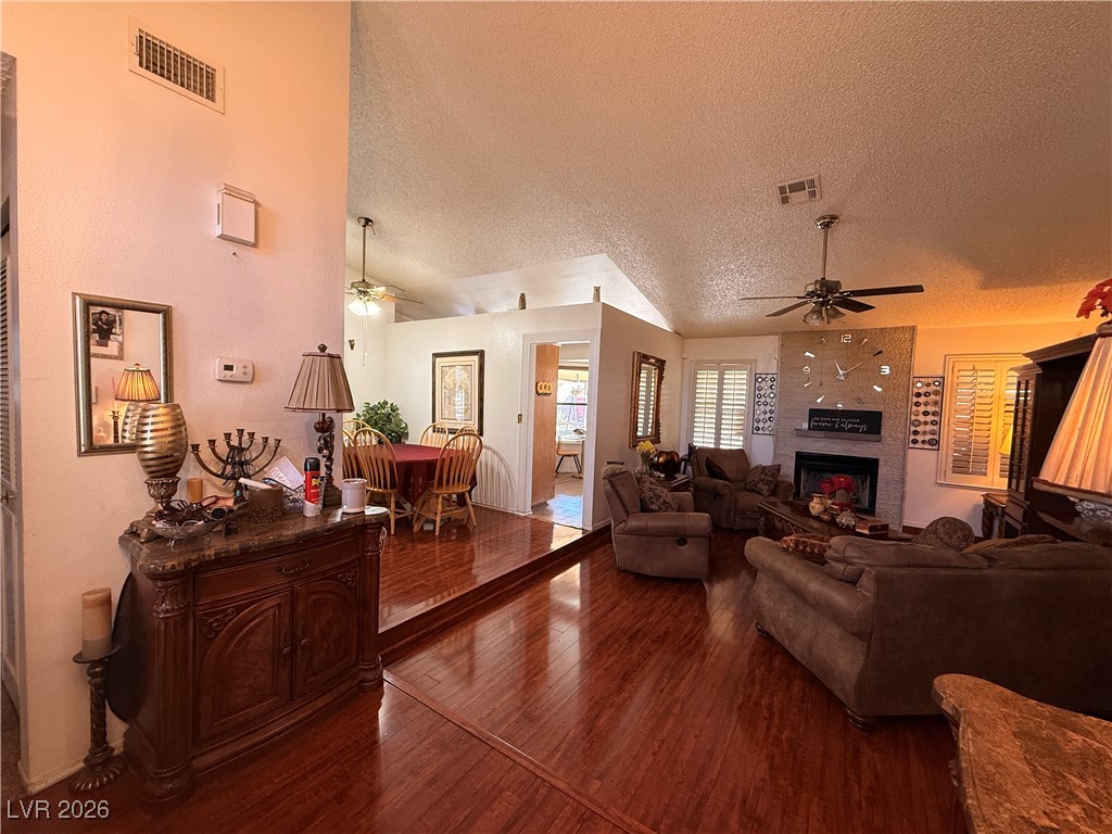 6425 West Eagle Point Road Las Vegas, NV 89108 - Photo 9 of 42 Living area with ceiling fan, dark wood-type flooring, a fireplace, a textured ceiling, and vaulted ceiling