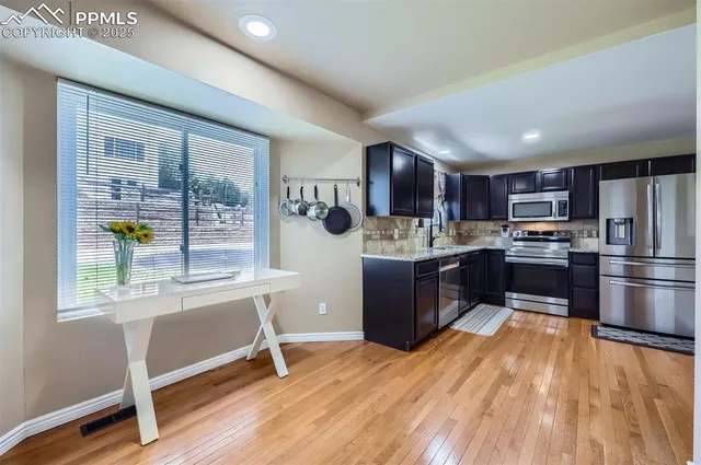 a kitchen with stainless steel appliances granite countertop a refrigerator a sink dishwasher a stove and a dining table with wooden floor